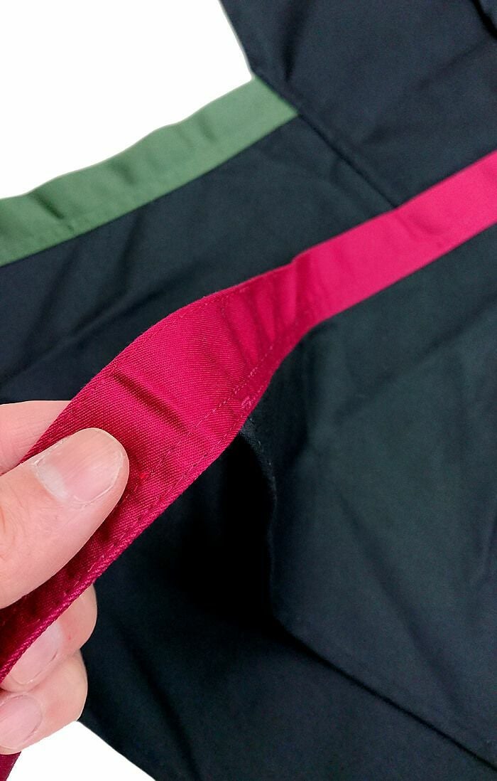 もう１枚同じ胸当てエプロンの生地をカットして、赤色と緑色の紐を作りあげて縫製しています。<br>もちろん弊社内の縫製スタッフ、もしくは近隣の縫製工場様のご協力で作り上げる事ができています。<br>よって縫製技術は高いので、ご安心ください。