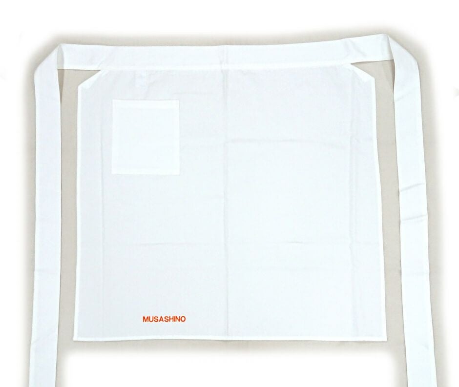 武蔵野栄養専門学校様に注文いただいた厨房エプロンにポケットを取り付けたお写真を紹介です。<br>綿100％の白エプロンはだいたいの場合、ポケットが付いていないものが多いです。<br>弊社でも取り扱い商品の中から探しましたが、やはりなかったので、ポケット取付加工をさせていただく事にいたしました！