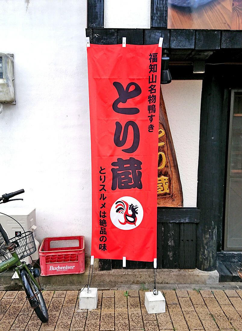 オリジナルのぼり旗が完成しましたので、こんな感じで店頭入口に設置いただきました。<br>やはりのぼりがあるのと無いのでは見た目の印象が全然違いますね。<br>のぼり旗がある方が断然、繁盛感の演出ができています！